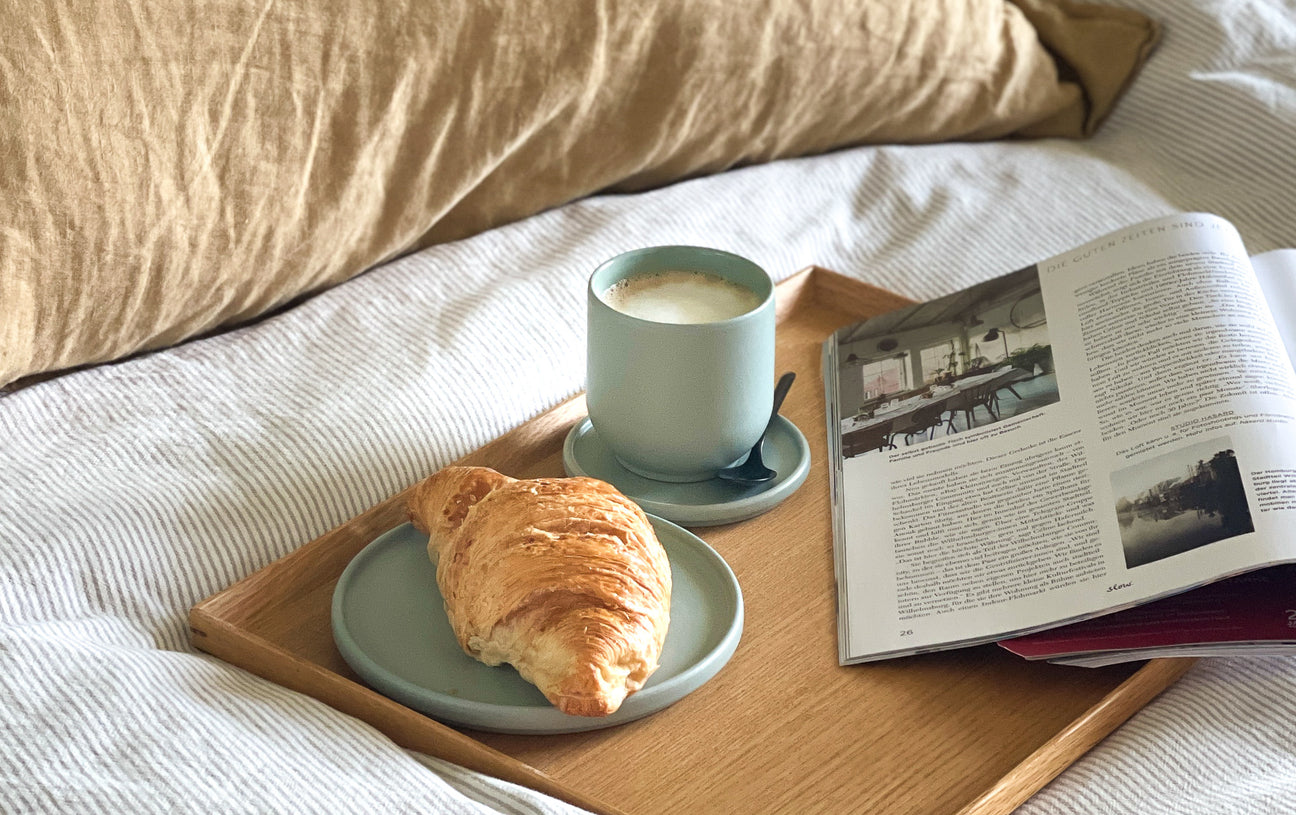 Frühstück im Bett mit Kaffeetasse und Teller mit Croissant
